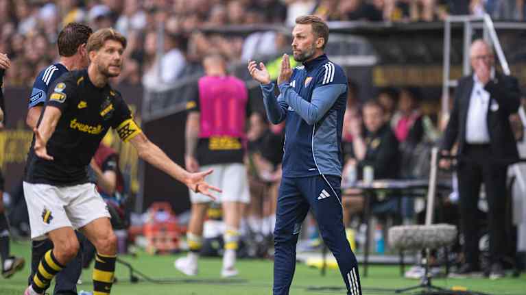 Kahden joukkueen intensiivinen ottelutunnelma kentällä, valmentajat ja pelaajat keskittyneinä pelin kulkuun.