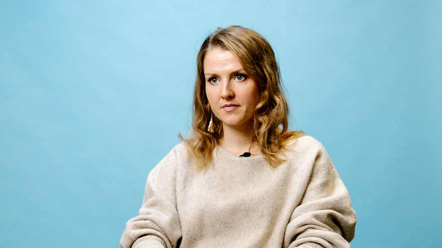 Henkilö istuu tuolilla sinertävän taustan edessä studiossa.