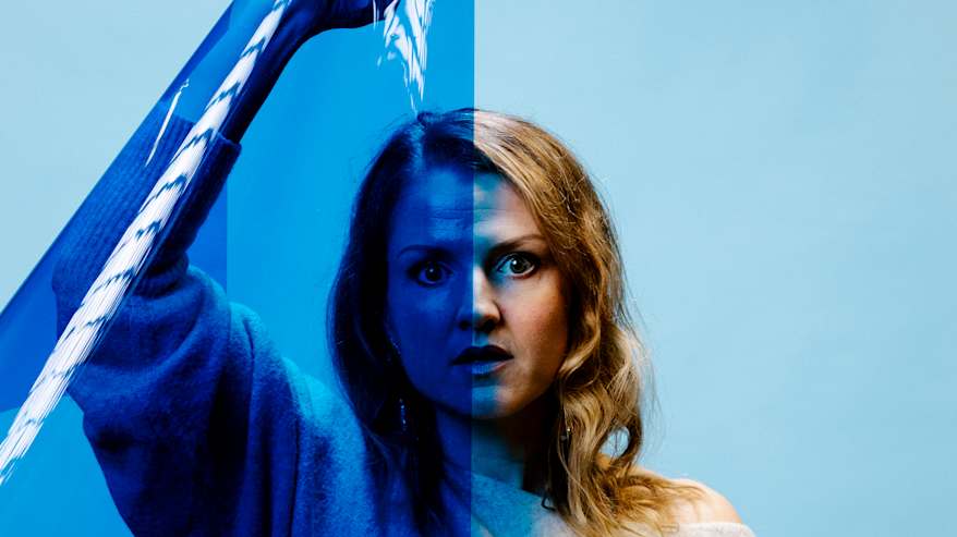 Henkilö seisoo sinertävän taustan edessä studiossa ja pitelee käsissään sinistä värikalvoa.