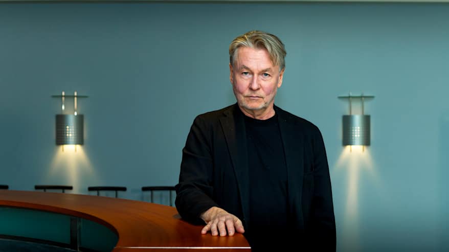 Mies seisoo pöydän vieressä pitäen kättä pöydän päällä.