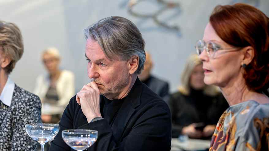 Mies istuu kahden naisen välissä pöydän ääressä. Pöydällä laseja.