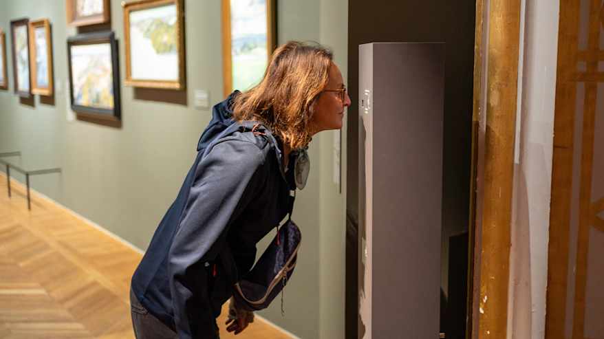 Nainen nuuhkii museossa hajutolppaa.