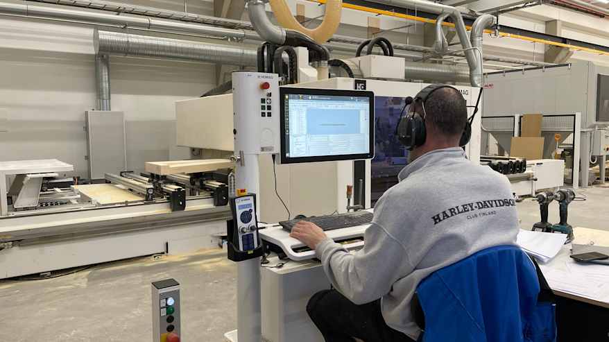 Puuverstaan työntekijä ohjaa tietokoneella jyrsintäkonetta. 