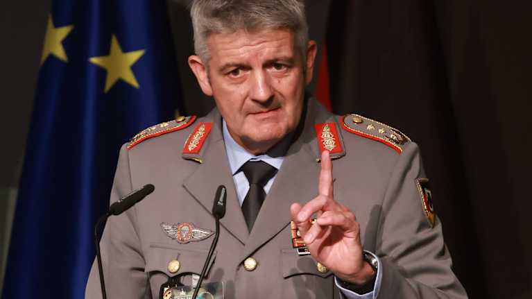 Alexander Sollfrank sotilasuniformussa, puhuu mikrofoniin toisen käden etusormi pystyssä.