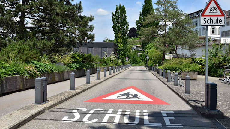 Katunäkymä Sveitsistä, asvaltissa varoitusmaalaus jossa lukee suomeksi koulu.