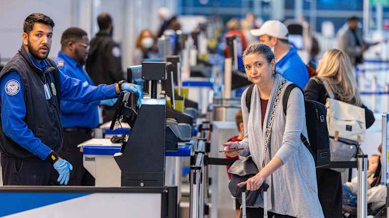 Ihmisiä matkatavaroiden kanssa jonossa virkailijan tiskille.