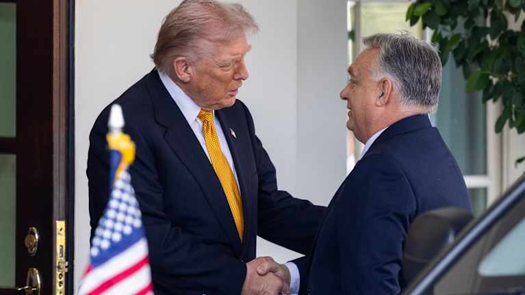 Donald Trump ja Viktor Orbánia kättelevät oven edessä. Etualalla Yhdysvaltain lippu mustassa autossa.