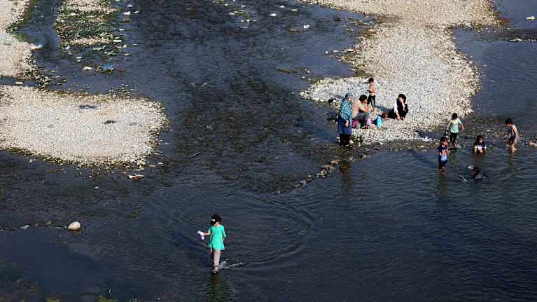 Ilmakuva ihmisistä ulkoilemassa vähävetisessä joen uomassa.
