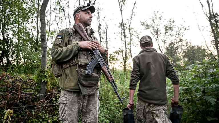 Kaksi ukrainalaista sotilasta on metsikössä. Toisella on edessään rynnäkkökivääri, toinen kantaa jotain.