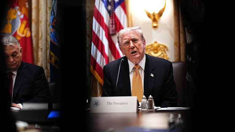 Trump puhuu, draamaattinen varjo, Orban kuuntelee. 