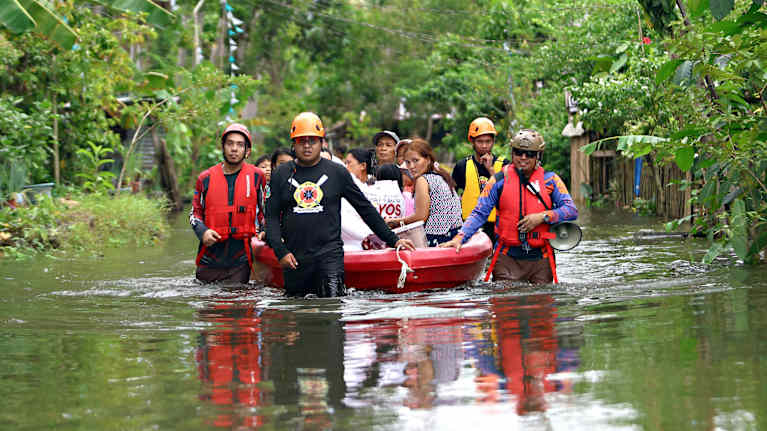 Ihmiset liiikkuvat veden valtaamalla tiellä pelastusveneen kanssa.