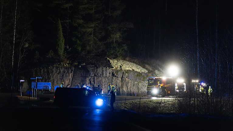 Pimeän aikaan tiellä poikittain pakettiauto, jossa sininen valo. Takana kallioleikkaus, jonka edessä ruttaantunut henkilöauto.
