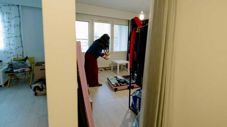 Henkilö pakkaa matkalaukkuaan olohuoneessa, jossa on pelkistetty sisustus. 