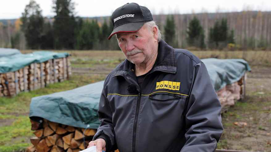 Harmaaseen haalariin pukeutunut mies pitää kädessään sinistä vihkoa.