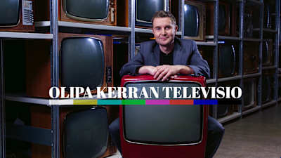 Juontaja Joonas Nordman nojaa punaiseen retro-televisioon, hänen takanaan on seinä täynnä vanhoja televisioita.