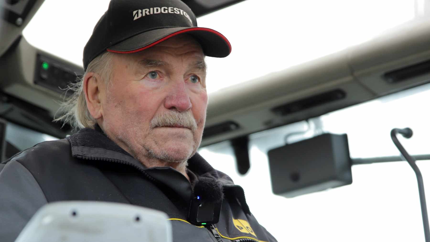 Harmaaseen työhaalariin pukeutunut mies istuu traktorin hytissä.