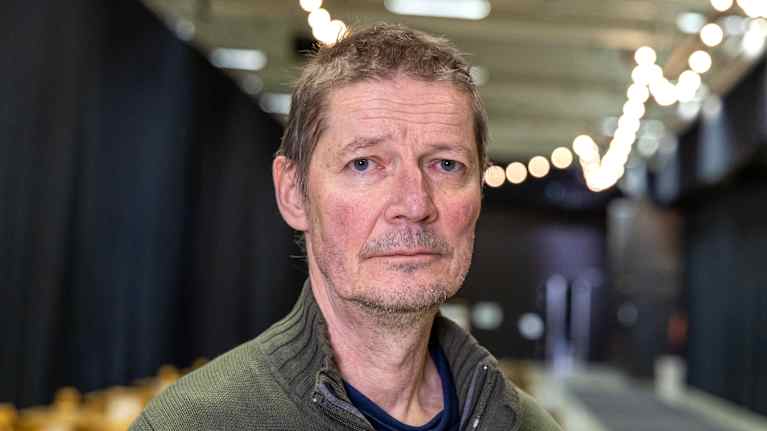 Miesohjaaja katsoo kameraan teatterin lämpiössä.