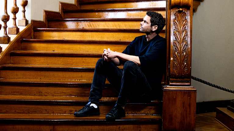 Peter Sarlin istuu puisella portaikon askelmalla nojaten kaiteeseen.