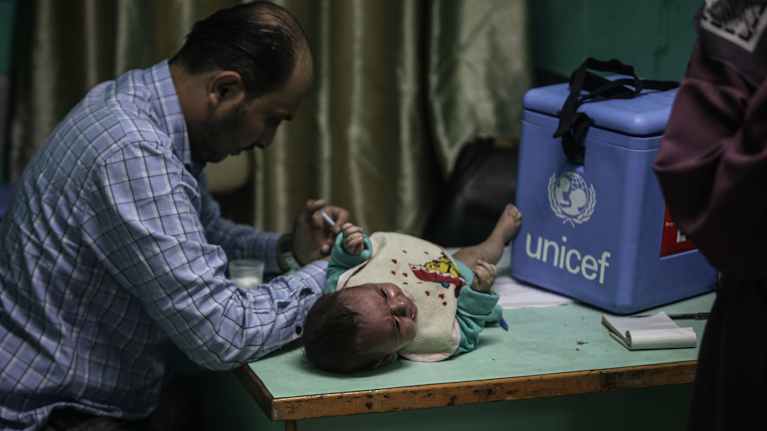 Lääkäri antaa rokotetta lapselle UNICEF-rokotusboksin vieressä.