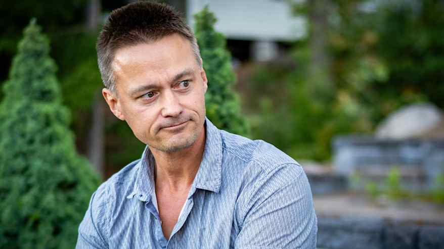 Jere Loikkanen istuu puutarhassa rentouttavassa ympäristössä, pukeutuneena sinisävyiseen ruutupaitaan. 