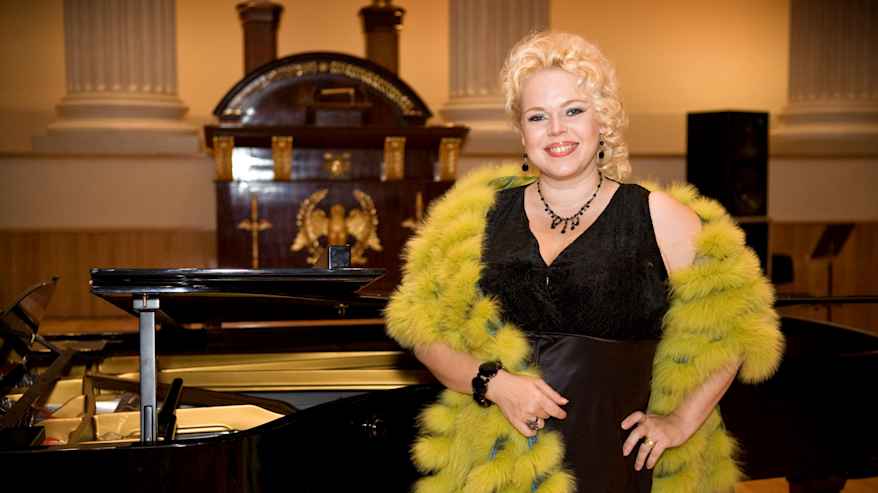 Johanna Rusanen-Kartano poseeraa mustassa iltapuvussa ja vihretävässä turkiksessa.