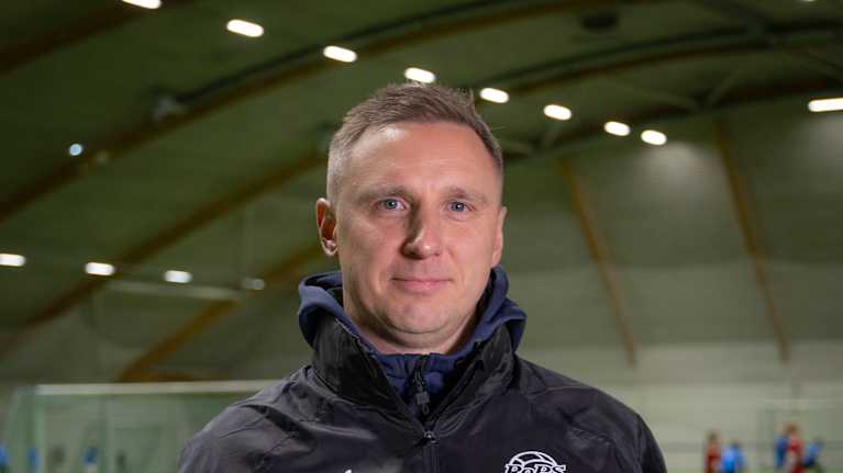 Mies poseeraa jalkapallokentällä pallon kanssa.