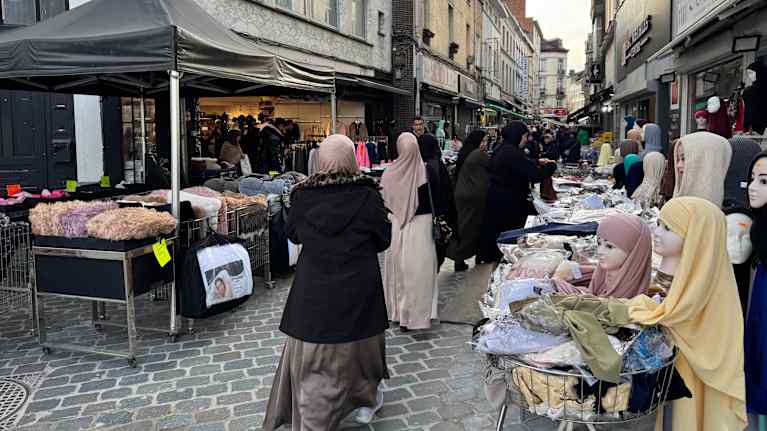 Jalankulkijoita ja vaatekojuja kapealla kadulla.