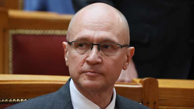 Sergei Kirijenko on lehterillä tummanharmaassa puvussa, kauluspaidassa ja tummassa kravatissa, silmälasit päässään.