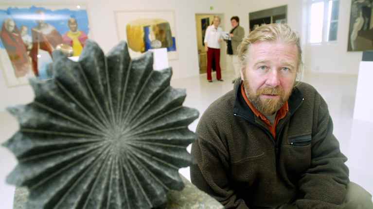 Matti Peltokangas poseeraa veistoksen vieressä.