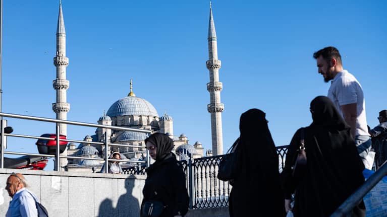 Ihmisiä kävelee kadulla. Taustalla Uusi Valide Sultanin moskeija ja sininen taivas.