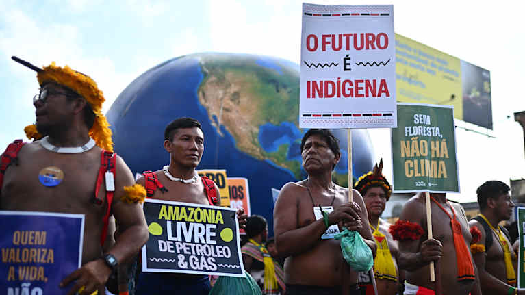 Alkuperäiskansoja seisoo kylttien kanssa mielenosoituksessa.