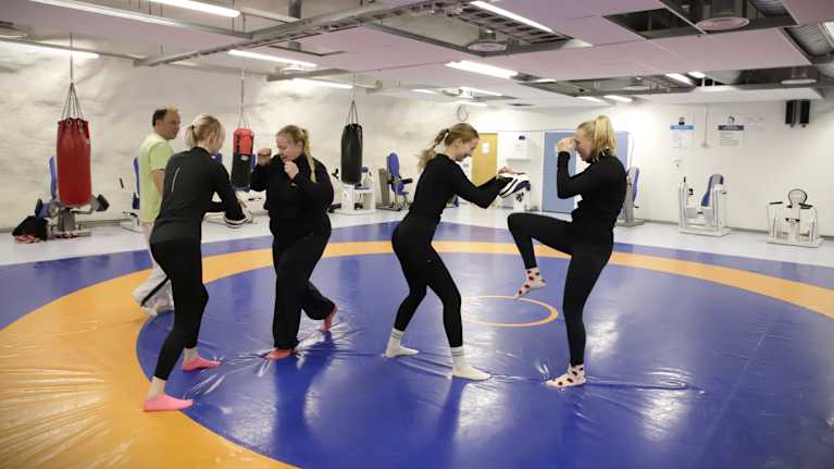Neljä naista harjoittelee itsepuolustusta painisalissa.