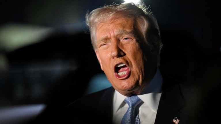 Donald Trump puhuu suu ammollaan lehdistölle virkakoneensa edustalla iltahämärässä.