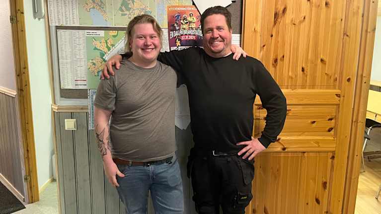 Isä ja poika seisoo ilmoitustaulun edessä kaulakkain.