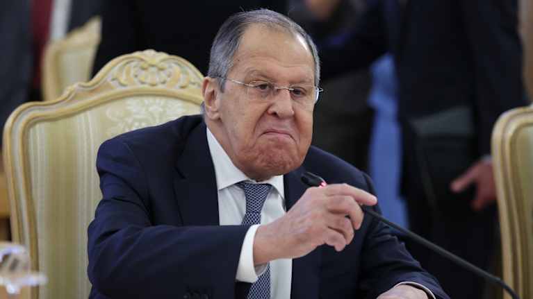 Sergei Lavrov istuu tummassa puvussa pöydän takana ja kääntää mikrofonia itseään kohti kasvoillaan hyvin yrmeä ilme.