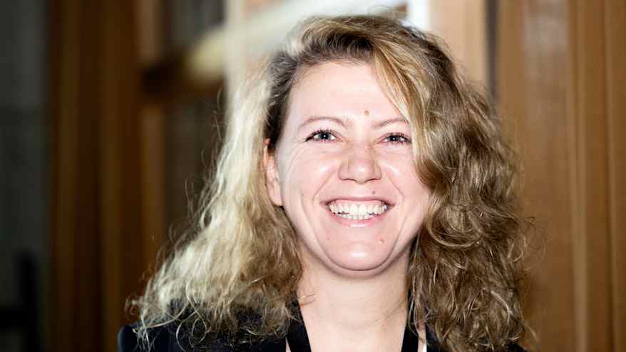 Kiharatukkainen nainen hymyilee leveästi.