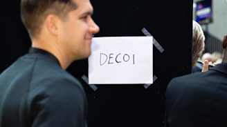 Aneljä paperi johon kirjoitettu tussilla DECOI teipattuna mustaan verhoon.