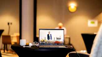 Läppärin näytöllä pyörii video ja taustalla istuu henkilö pöydän ääressä.