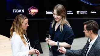 KOlme ihmistä joista yksi ojentaa toiselle kauko-ohjainta.