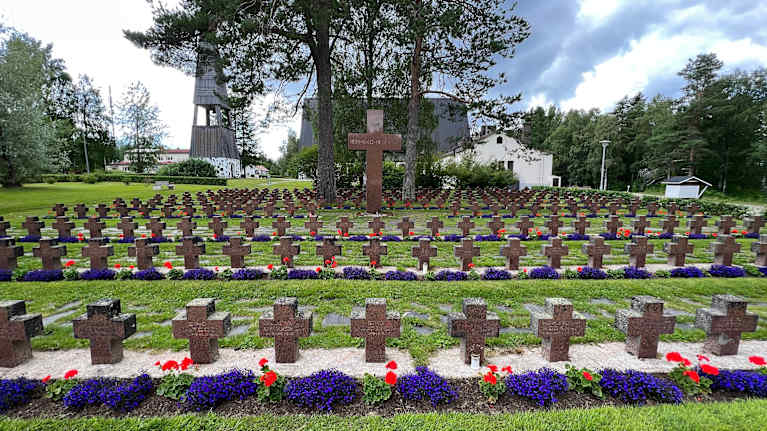 Kymmeniä punagraniittisia ristejä sankarihautojen merkkinä vihreän ruohon peittämällä hautausmaalla.