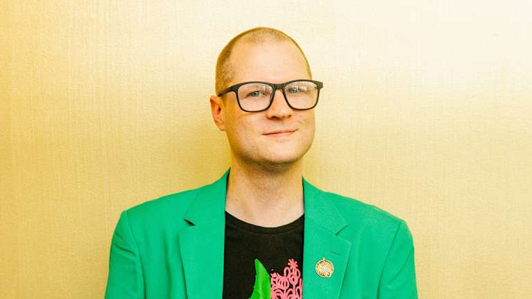 Henkilö pukeutuneena kirkkaan vihreään pukuun ja mustaan Wicked t-paitaan.