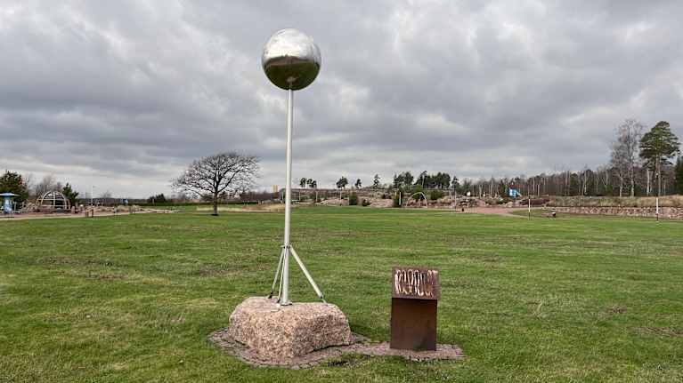 Puistossa on tolpan päässä oleva pallo, joka kuvaa aurinkoa. Vieressä teline, josta opastaulu on revitty irti.