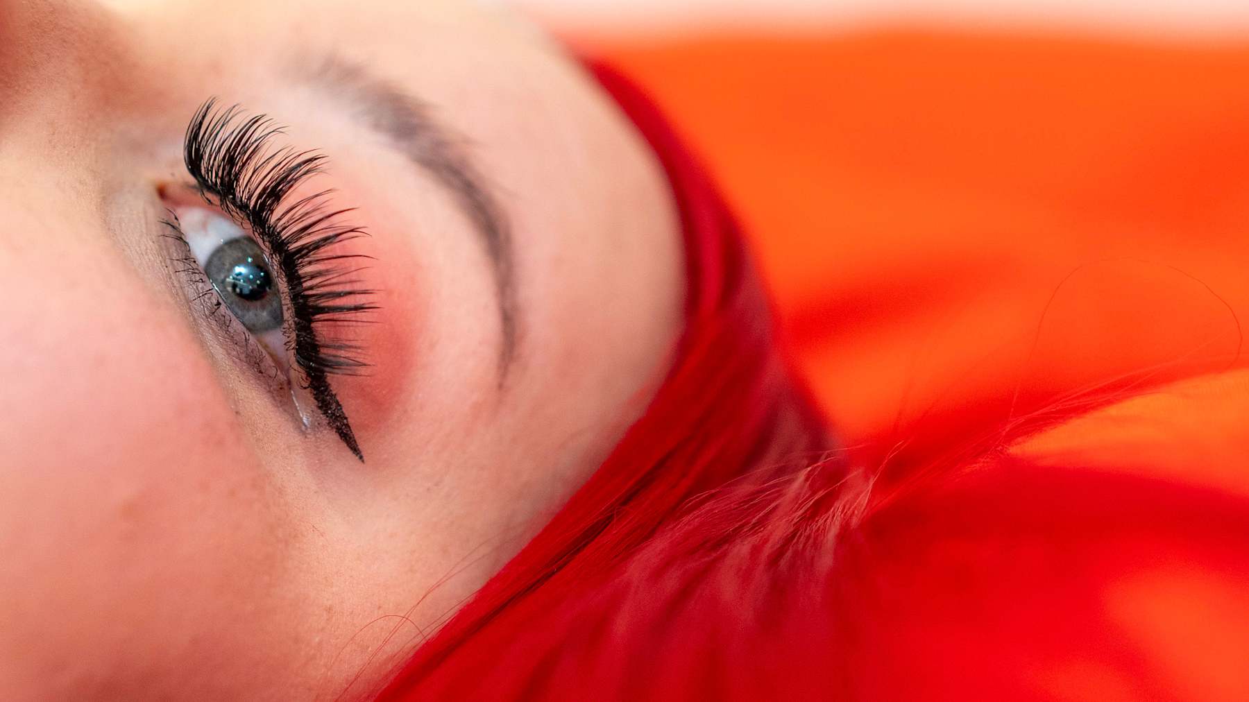 Kuvassa näkyy lähikuvassa Jenna Sirkiän silmä sekä kirkkaan punainen tausta ja punaiset hiukset, jotka korostavat eläväisiä värejä.
