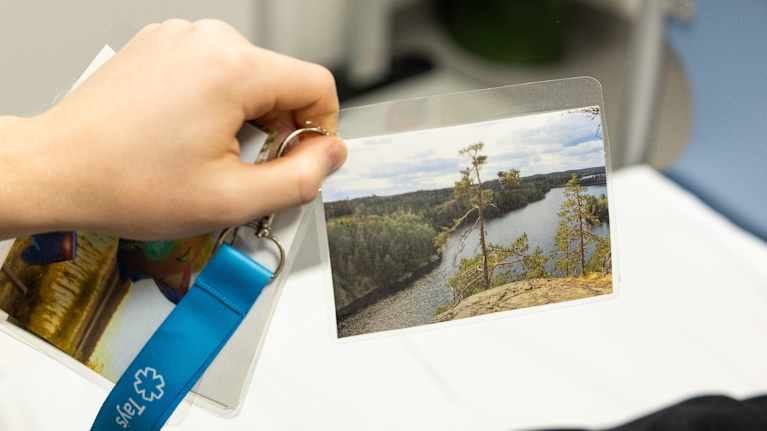 Akseli Vahila pitää kädessään kuvaa, jossa on maisema jyrkänteeltä, taustalla metsää kesällä.
