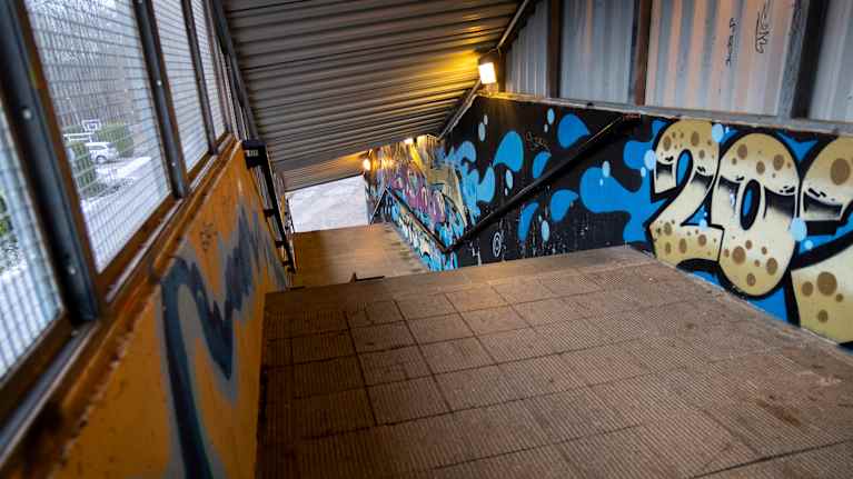 Betonisen ulkoportaikon reunoilla ja seinissä on värikkäitä sinisiä, mustia ja kultaisia graffiteja. Katto on aaltopeltiä.