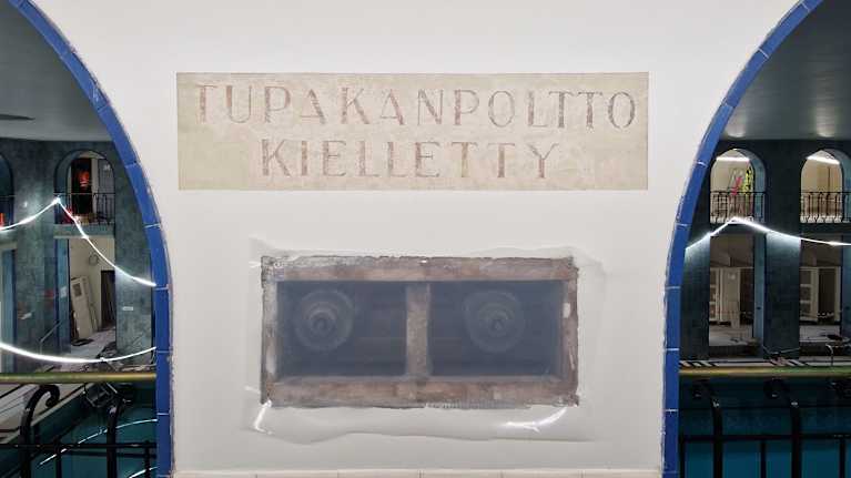 Remontissa seinästä paljastunut vanha Tupakanpoltto kielletty -kyltti Yrjönkadun uimahallin sisäseinässä.
