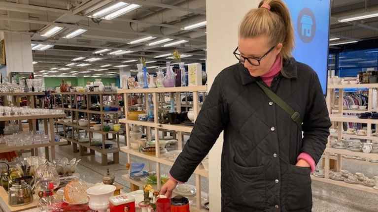 Nainen katselee kirpputorilla pöydällä olevia astioita. Astiat ovat punavalkoisia.