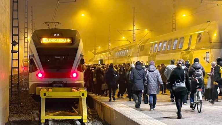 Junia ja joukko ihmisiä juna-aseman laiturilla.