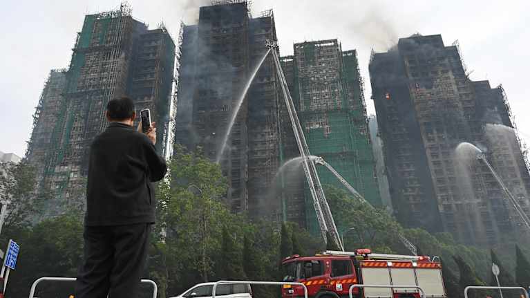 Mies ottaa kuvaa puhelimellaan mustaksi palaneista ja savuavista tornitaloista.