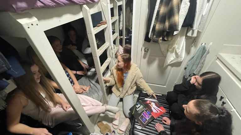 Kuvassa muutaman neliön kokoinen asunto, jossa istuu kuusi naista.